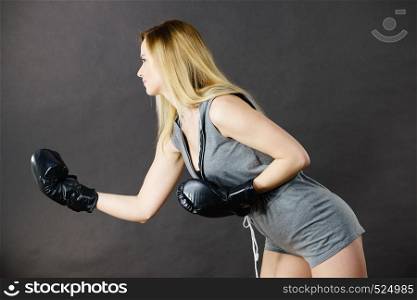 Sportsmanship fairplay and strong body. Young woman fighting boxing. Blonde girl wearing black punch gloves. Sport and fitness, power, exercising, side view on gray. Boxer girl exercise with boxing gloves.