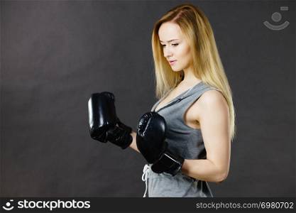 Sportsmanship fairplay and strong body. Young woman fighting boxing. Blonde girl wearing black punch gloves. Sport and fitness, power, exercising, side view on gray. Boxer girl exercise with boxing gloves.