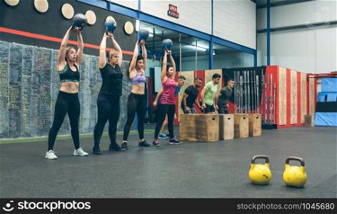 Sportswomen exercising with kettlebells and sportsmen doing box jumps. Sportswomen with kettlebells and sportsmen in background