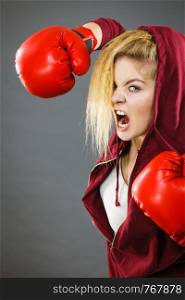 Sporty angry determined woman wearing red boxing gloves, fighting and screaming. Studio shot on dark background.. Angry woman wearing boxing gloves