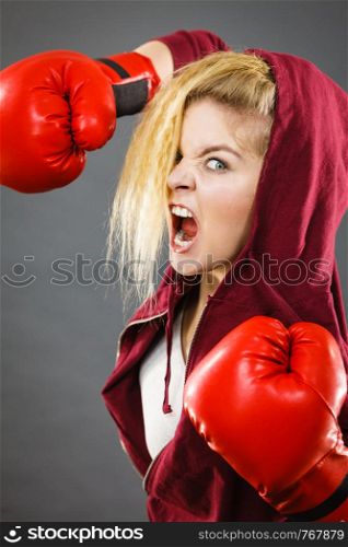 Sporty angry determined woman wearing red boxing gloves, fighting and screaming. Studio shot on dark background.. Angry woman wearing boxing gloves