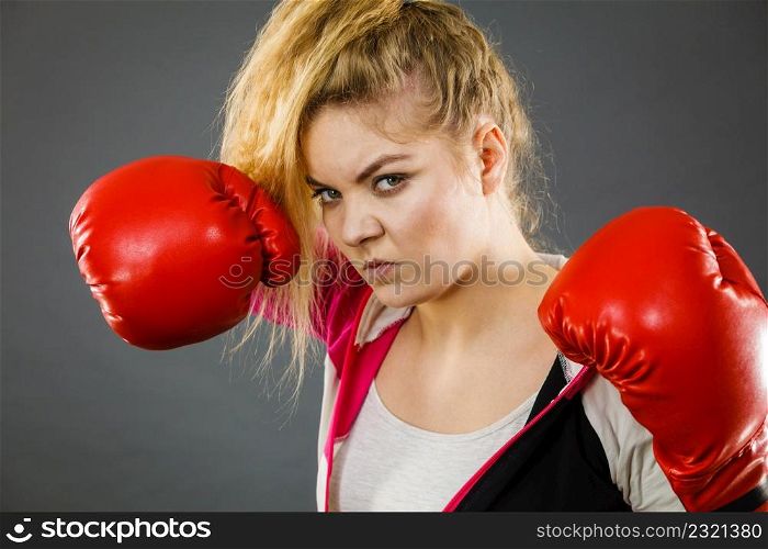 Sporty angry determined woman wearing red boxing gloves, fighting. Studio shot on dark background.. Angry woman wearing boxing gloves