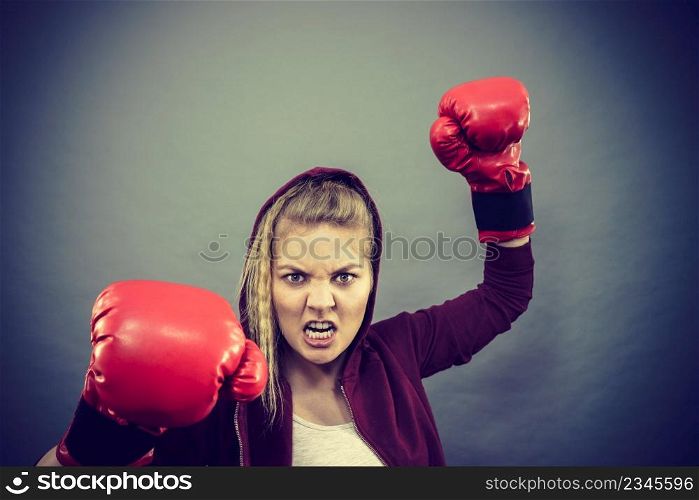 Sporty angry determined woman wearing red boxing gloves, fighting. Studio shot on dark background.. Angry woman wearing boxing gloves