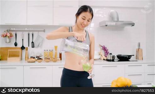 Sporty Asian woman drinking apple juice in the kitchen, beautiful female in sport clothing use organic fruits lots of nutrition making apple juice by herself at home. Healthy food concept.