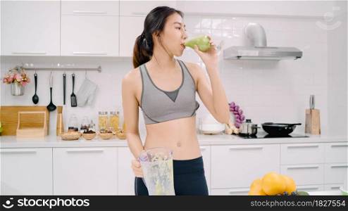 Sporty Asian woman drinking apple juice in the kitchen, beautiful female in sport clothing use organic fruits lots of nutrition making apple juice by herself at home. Healthy food concept.