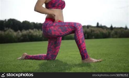 Sporty beautiful woman practicing yoga, doing kneeling hip flexor stretch exercise on green grass outside in the park