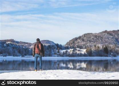 Sporty Caucasian man is at the lakeshore, enjoying the view. Winter landscape.