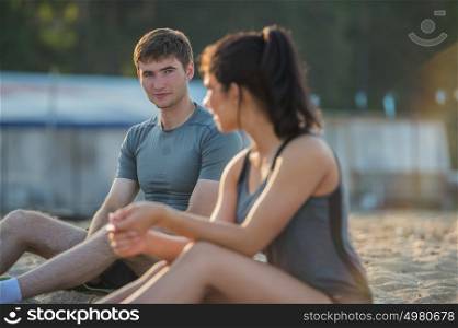 Sporty couple resting after workout on beach during sunset