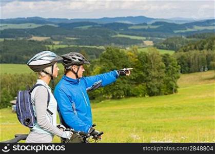 Sporty cyclist couple, man pointing to beautiful landscape