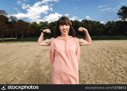 Sporty energetic athletic woman wears pink sports top smiles as shows her biceps, likes sport and active lifestyle. People, health and physical activity concept. The guy behind the girl shows a biceps. Sporty energetic athletic woman wears pink sports top smiles as shows her biceps, likes sport and active lifestyle.