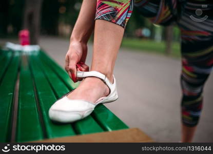 Sporty female person buttons footwear, sport bottle and towel on the bench on background. Woman in sportswear on fitness training