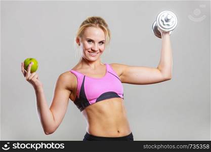 Sporty fit woman holding heavy dumbbells weights in one and apple fruit in another hand. Fitness bodybuilding and healthy dieting concept.. Diet fit body. Girl holds dumbbells and apple fruit