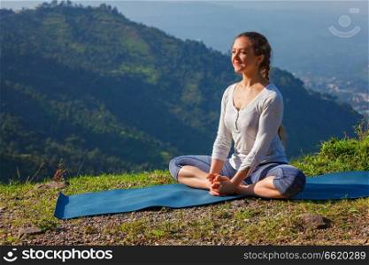 Sporty fit woman practices yoga asana Baddha Konasana - bound angle pose outdoors in HImalayas mountains in the morning with sky. Himachal Pradesh, India. Sporty fit woman practices yoga asana Baddha Konasana outdoors
