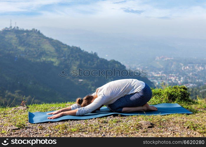 Sporty fit woman practices yoga asana Balasana - child pose outdoors in mountains. Sporty fit woman practices yoga asana Balasana