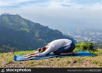 Sporty fit woman practices yoga asana Balasana - child pose outdoors in mountains. Sporty fit woman practices yoga asana Balasana