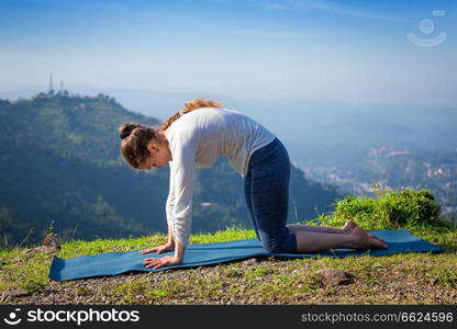 Sporty fit woman practices yoga asana Marjariasana - cat pose outdoors in Himalayas. Woman practices yoga asana Marjariasana outdoors