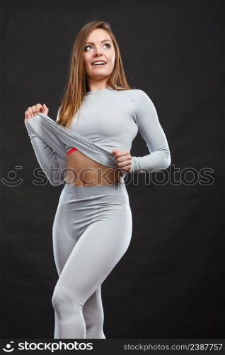 Sporty fitness shape garments concept. Attractive lady in thermal clothes. Young seductive girl pulling shirt showing skin presenting thermoactive clothing on black. Sport fit woman in thermal clothes.