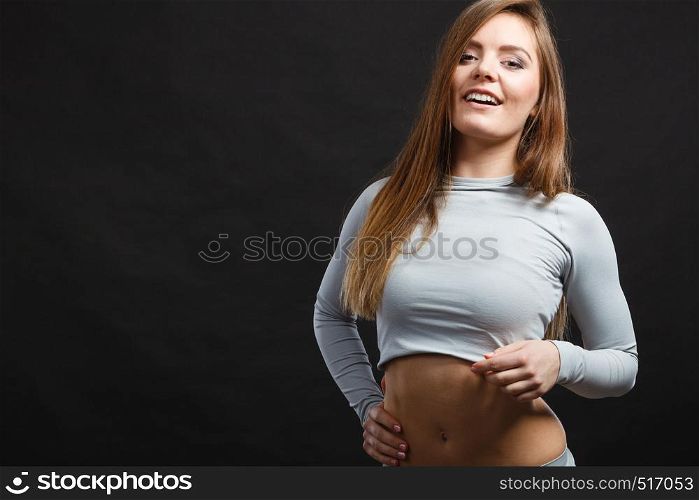 Sporty fitness shape garments concept. Attractive lady in thermal clothes. Young seductive girl pulling shirt showing skin presenting thermoactive clothing on black. Sport fit woman in thermal clothes.