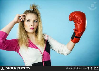 Sporty funny woman wearing red boxing glove gesturing and being confused. Studio shot on blue background.. Funny confused woman wearing boxing glove