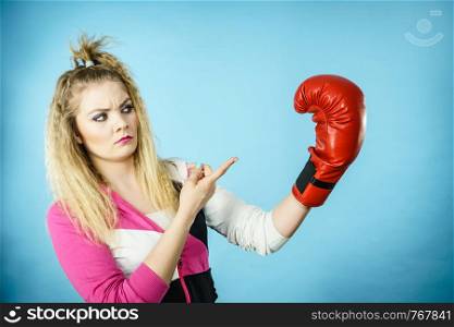 Sporty funny woman wearing red boxing glove gesturing and being confused. Studio shot on blue background.. Funny confused woman wearing boxing glove