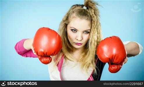 Sporty funny woman wearing red boxing gloves, trying to fight. Studio shot on blue background.. Funny woman wearing boxing gloves