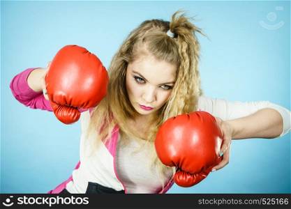 Sporty funny woman wearing red boxing gloves, trying to fight. Studio shot on blue background.. Funny woman wearing boxing gloves