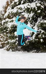 Sporty girl jumping in snow with trees in background. Winter sports, outdoor fitness, nature workout, health concept.. Winter sport, girl jumping in snow