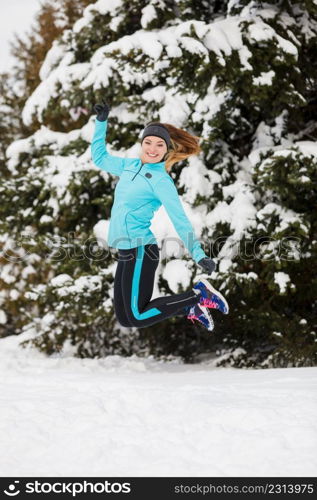 Sporty girl jumping in snow with trees in background. Winter sports, outdoor fitness, nature workout, health concept.. Winter sport, girl jumping in snow