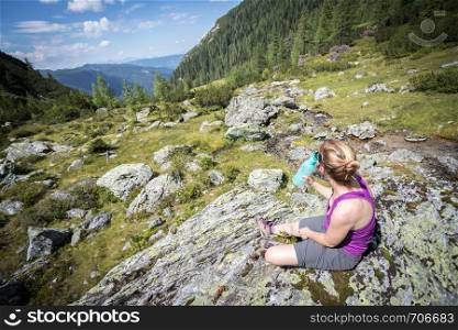 Sporty girl on a hiking trip is sitting on a rock an enjoys the idyllic mountain landscape