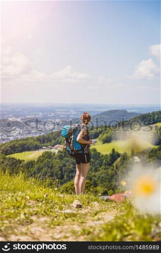Sporty girl on a hiking trip is standing on the meadow an enjoying the view over the far away city