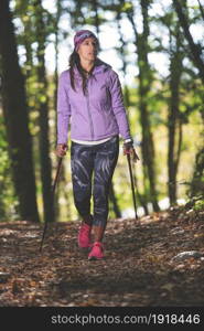 Sporty girl practicing nordic walking on the path in the forest road