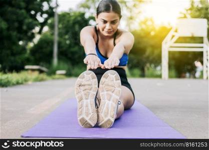 Sporty girl stretching her legs sitting on a mat in a park. Athlete woman sitting doing leg stretch in a park. Athlete girl sitting on a mat stretching her legs in a park