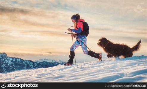 Sporty girl with her dog during an alpine trekking on the snow
