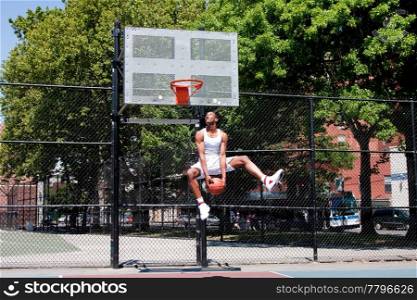 Sporty handsome African-American man dressed in white jumping in the air reaching for the basket while playing basketball in an outdoor court on a summer day