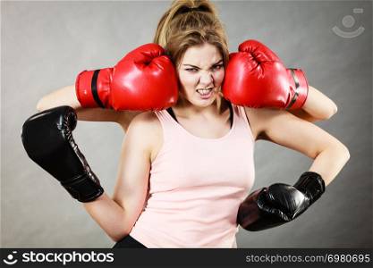 Sporty having head between boxing gloves, somebody punching her. Studio shot on grey background.. Woman having head between boxing gloves