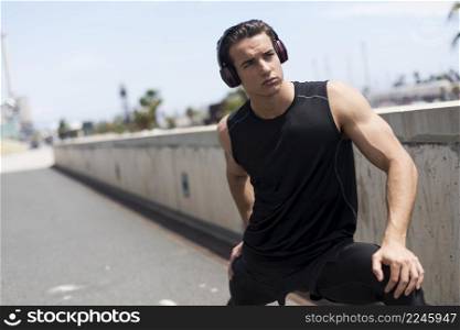 Sporty male with headphones stretching his legs outdoors.