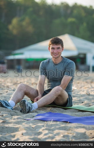 Sporty man resting after workout on beach during sunset