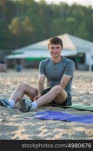 Sporty man resting after workout on beach during sunset