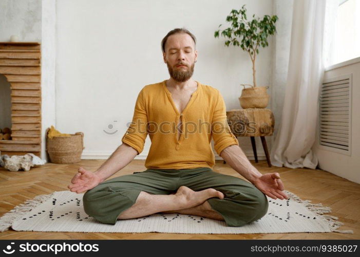 Sporty mindful man meditating alone at home apartment. Peaceful calm hipster guy practicing yoga in lotus pose indoors holding hands in mudra. Sporty mindful man meditating alone at home apartment