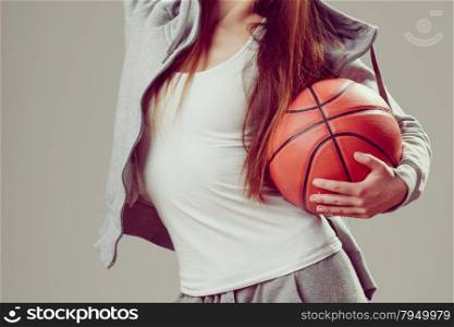 Sporty teen girl in hood holding basketball. . Closeup of sporty teenager girl body wearing hooded sweatshirt holding basketball. Teen sport.
