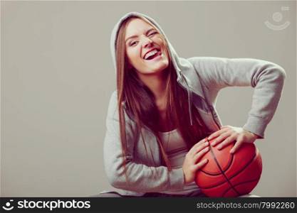 Sporty teen girl in hood holding basketball. . Funny sporty teenager girl wearing hooded sweatshirt holding basketball. Teen sport. Face expression.
