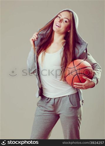 Sporty teen girl in hood holding basketball. . Happy sporty teenager girl wearing hooded sweatshirt holding basketball. Teen sport.
