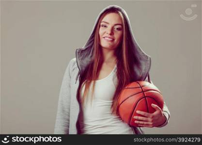 Sporty teen girl in hood holding basketball. . Happy sporty teenager girl wearing hooded sweatshirt holding basketball. Teen sport.