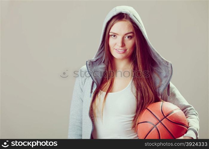 Sporty teen girl in hood holding basketball. . Sporty teenager girl wearing hooded sweatshirt holding basketball. Teen sport.