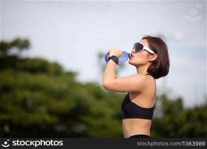 Sporty woman asian drinking water outdoor after running on sunny day