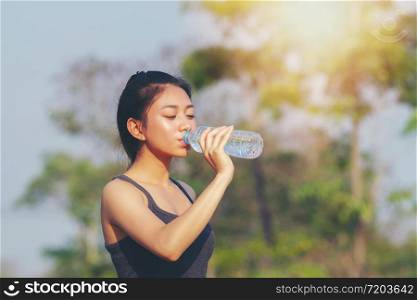 Sporty woman asian drinking water outdoor on sunny day