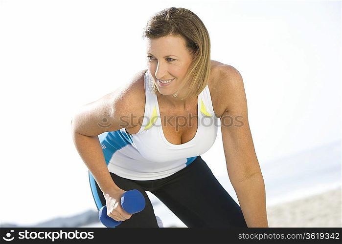Sporty woman at the beach lifting hand weights