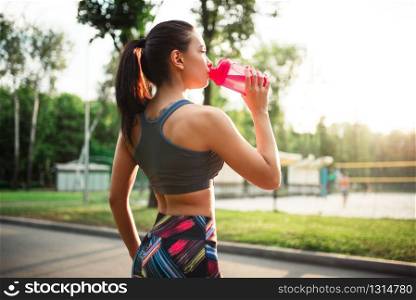 Sporty woman drink water from sport bottle, training in summer park. Girl on outdoors workout. Woman drink water from sport bottle