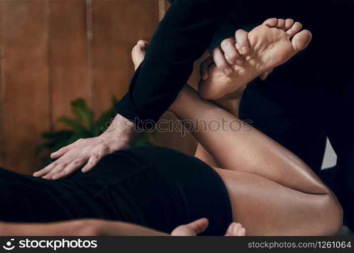 Sporty woman enjoying shiatsu legs massage, lying on the wooden floor, wearing black clothes