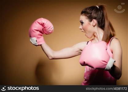 Sporty woman female boxer model wearing big fun pink gloves playing sports boxing studio shot, brown background